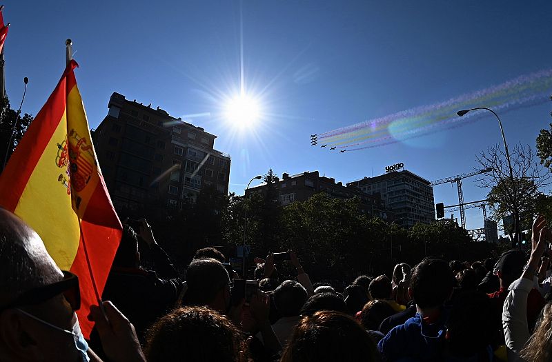 Asistentes al desfile militar en el Paseo de la Castellana observan las acrobacias de la Patrulla Águila en el cielo.