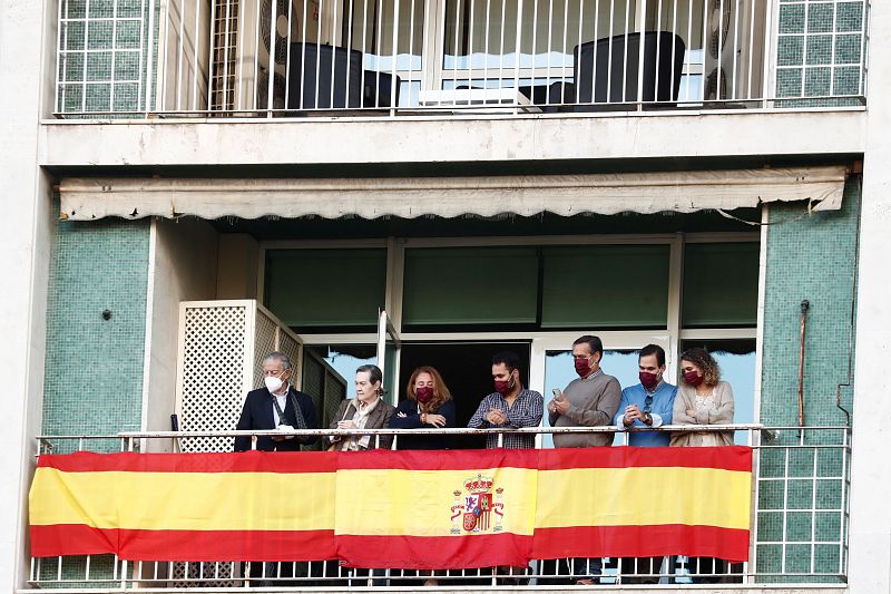 Una familia observa desde el balcón de su casa, decorado con una bandera de España, el desfile de las fuerzas armadas en el Día de la Hispanidad.