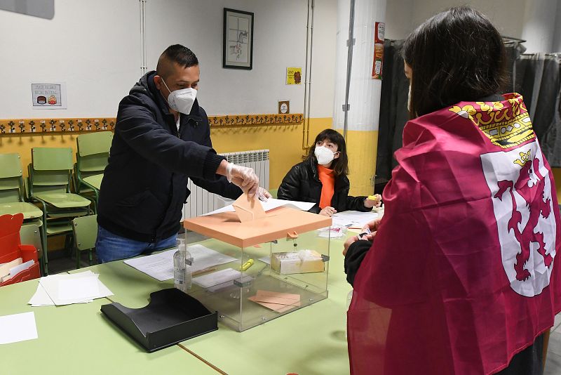 Una joven con una bandera de León atada a su cuello vota en el colegio electoral instalado en la guardería municipal de Cistierna (León)