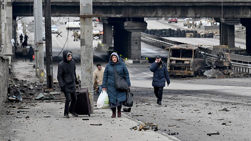 Unas personas cargan con sus pertenencias junto a los escombros de los combates en Kiev