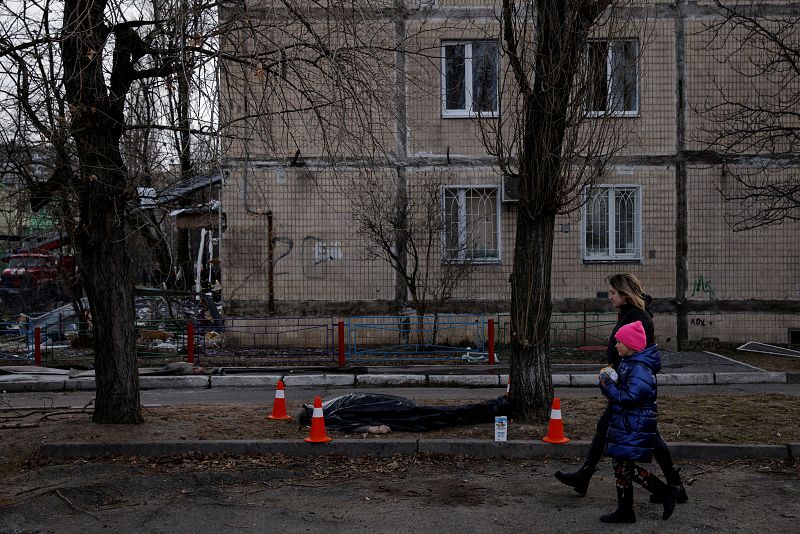 Una mujer y una niña pasan por delante de una persona muerta ante el edificio residencial atacado por las tropas rusas este lunes, en el distrito de Obolon de Kiev