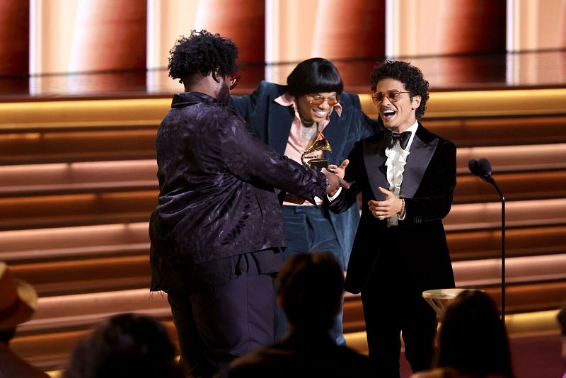 Anderson Paak (C) y Bruno Mars (R) aceptan el premio Canción del año por 'Leave The Door Open' de Questlove (L) en el escenario.