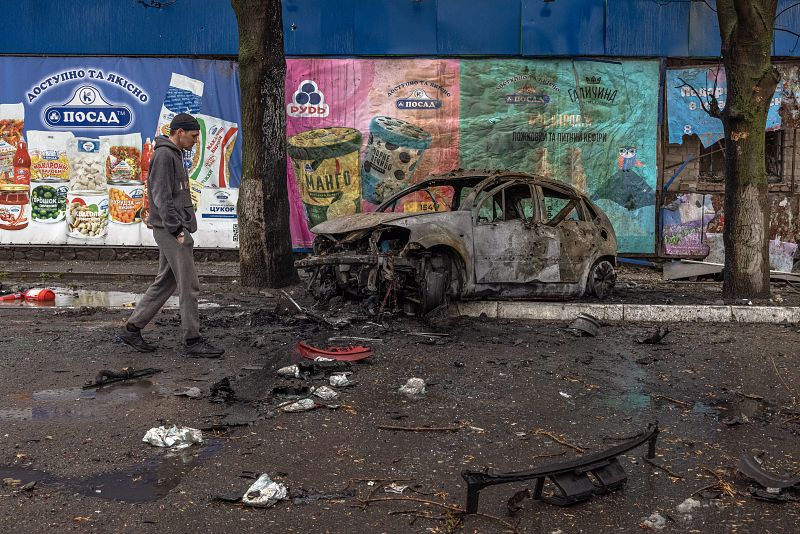 Un hombre pasa por delante de un coche quemado en la zona residencial que fue alcanzada por los bombardeos de la artillería rusa, en Járkov, al noreste de Ucrania