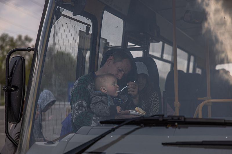 Un hombre da de comer a un niño en un autobús tras llegar de la ciudad de Orikhiv, en el punto de evacuación de Zaporiyia.