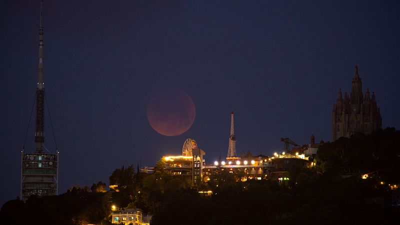 Vista del eclipse total de Luna tras el parque de atracciones del Tibidabo.