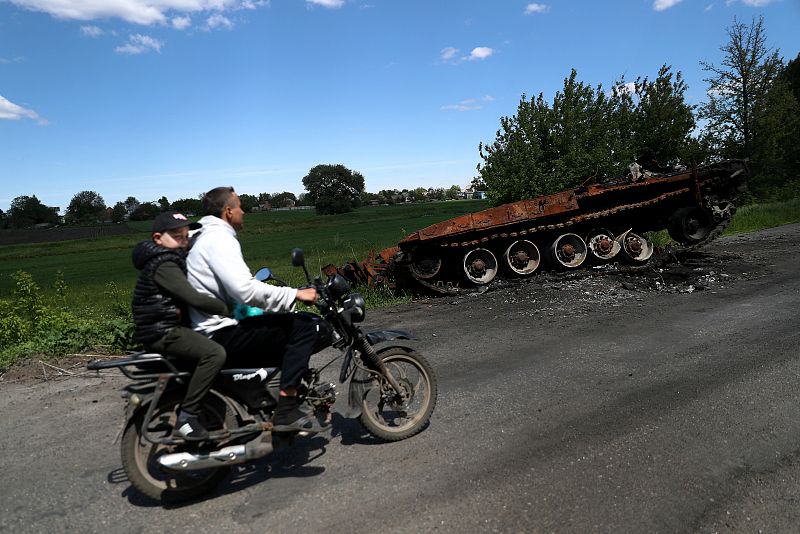 Residentes locales pasan en moto por delante de un tanque ruso destruido, mientras continúa el ataque de Rusia a Ucrania, en Chupakhivka