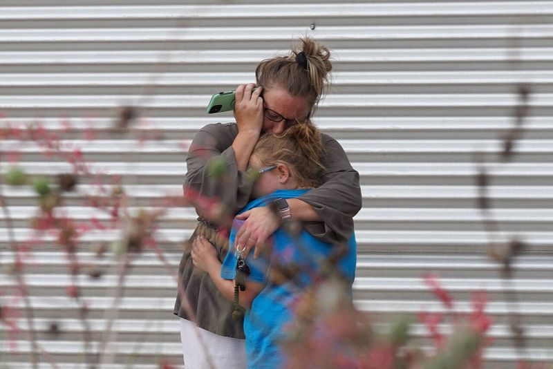 Una mujer llora y abraza a una niña mientras habla por teléfono a las puertas del Centro Cívico Willie de Leon, en Uvalde, Texas.