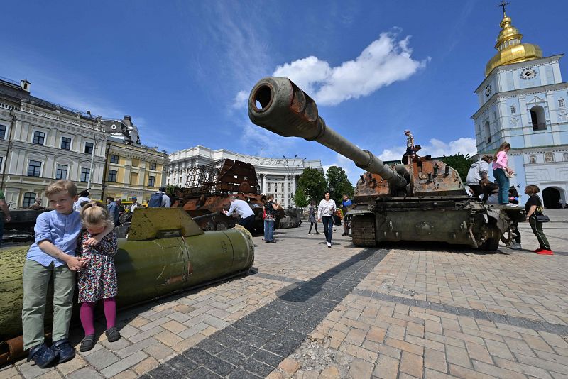 Dos niños se sientan sobre un fragmento de cohete ruso Tochka-U junto a un tanque dañado en la exposición al aire libre de material ruso destruido en el centro de Kiev.