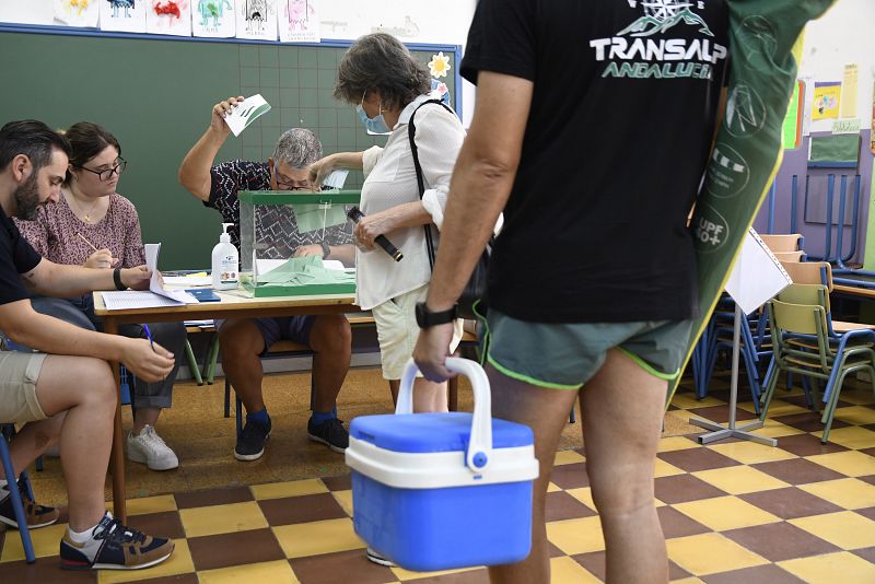 Un hombre cargado con nevera y sombrilla de playa espera para ejercer su derecho al voto en el colegio Virgen del Mar de Almería