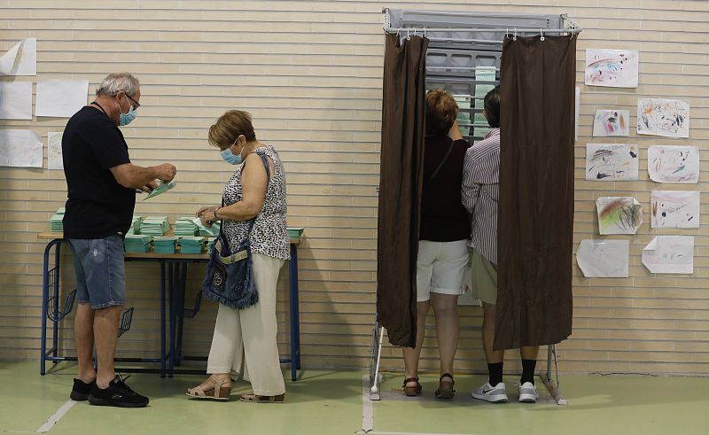 Varias personas cogen papeletas para ejercer su derecho al voto en el CEIP Malala de Mairena del Aljarafe en Sevilla