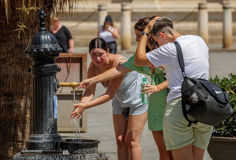 Unas turistas se refrescan en una fuente de agua junto a la Catedral de Sevilla.
