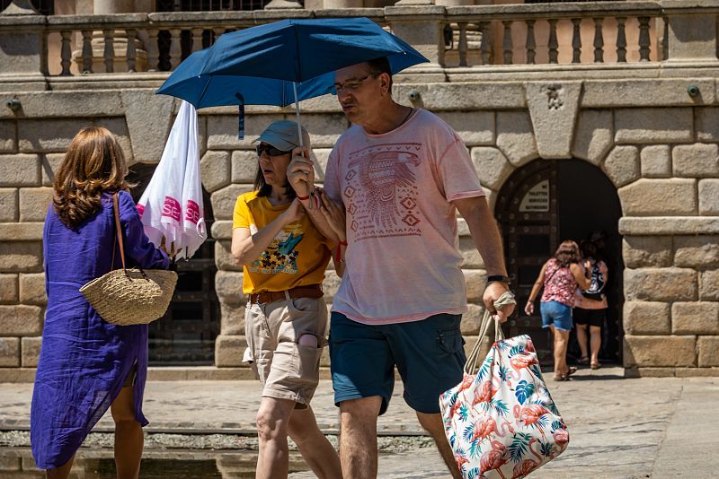 Varias persona caminando el domingo bajo un paragüas por una calle de Toledo.