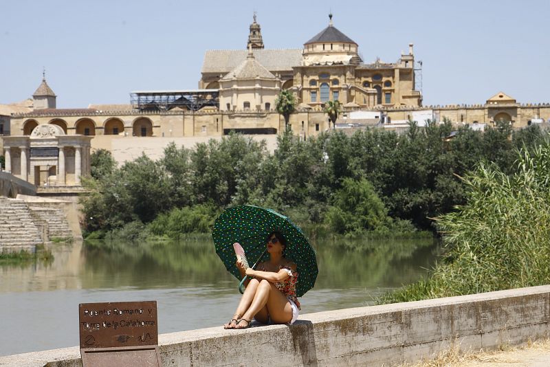 Una turista se protege del calor con un paraguas y un abanico a la orilla del río Guadalquivir cerca de la Mezquita-Catedral de Córdoba.