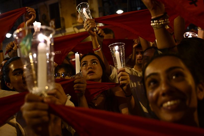 Los pamploneses, vestidos de blanco y rojo, sostienen velas y pañuelos mientras cantan la canción de San Fermín 'Pobre de Mi'