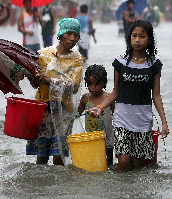 Una familia filipina cruzan una calle inundada por torrenciales lluvias en Las Pinas, sur de Manila