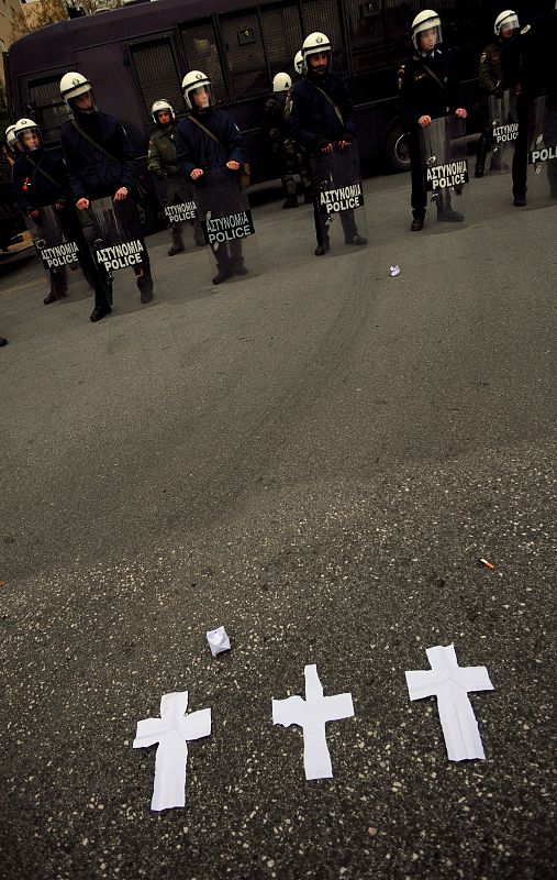 Tres cruces de papel permanecen en el asfalto frente a un grupo de antidisturbios.