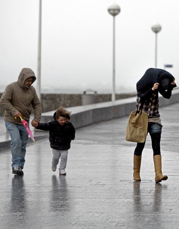 Varias personas tratan de protegerse hoy en el paseo de La Zurriola de San Sebastián, donde tras varios días, ha vuelto la lluvia acompañada de rachas de viento de 90 kilómetros por hora.