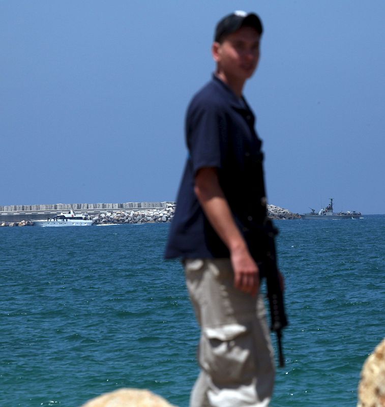 Un guardia de seguridad israelí evita el acceso de la prensa a la base militar del puerto de Ashdod (Israel) mientras un barco israelí escolta a tierra a uno de los barco de la "Flotilla de la Libertad".