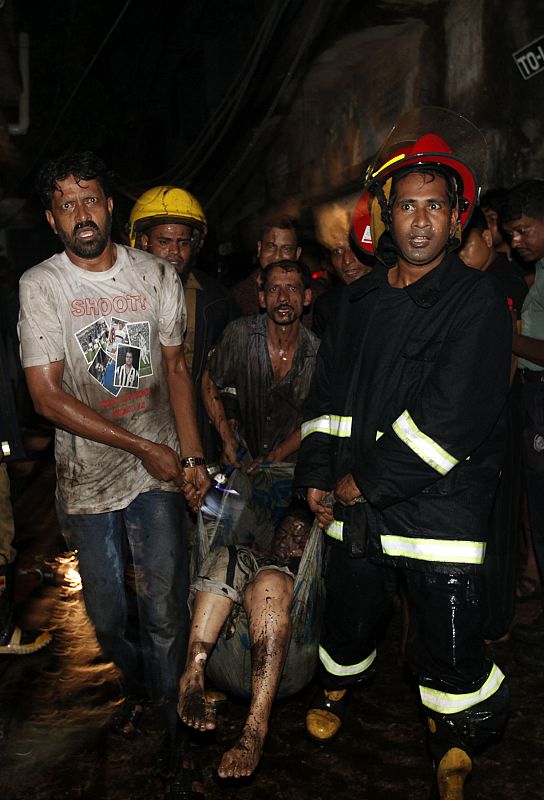Locals and fire-fighters recover the body of a victim from the site of a fire in the old part of Dhaka