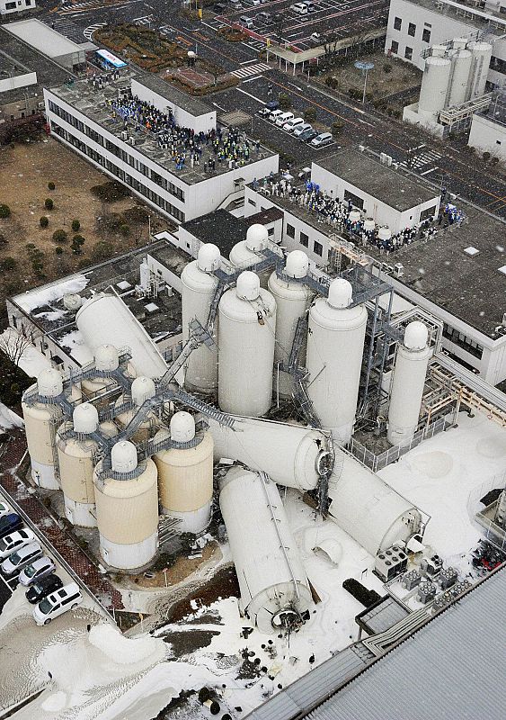 Evacuated employees are pictured near toppled tanks a brewery in Sendai, Miyagi Prefecture, northeastern Japan