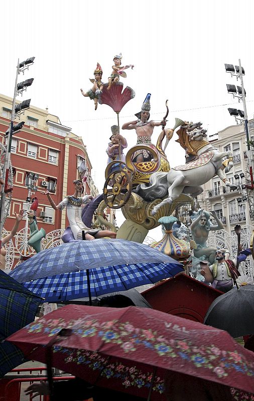 Un grupo de personas se protege de la lluvia mientras ve la falla Sueca-Literato Azorín, en Valencia