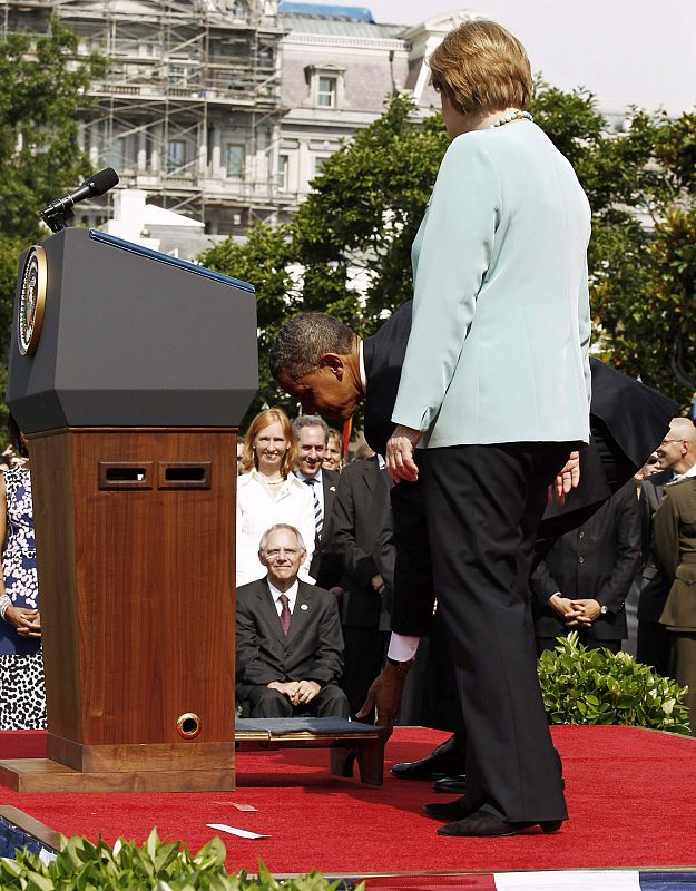 Obama coloca un escabel ante el atril para la canciller alemana.