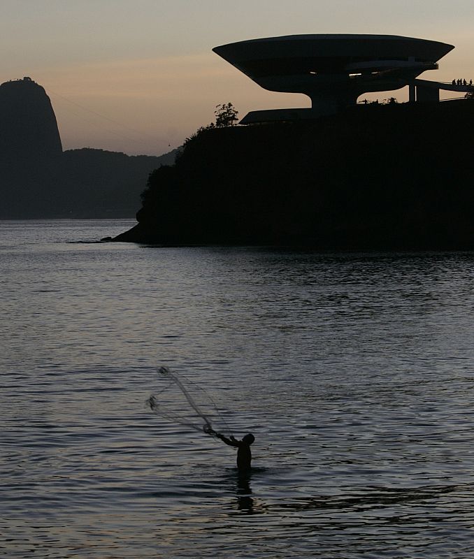 File photo of a fisherman throwing his net in front of the Contemporary Art Museum designed by architect Oscar Niemeyer in Niteroi
