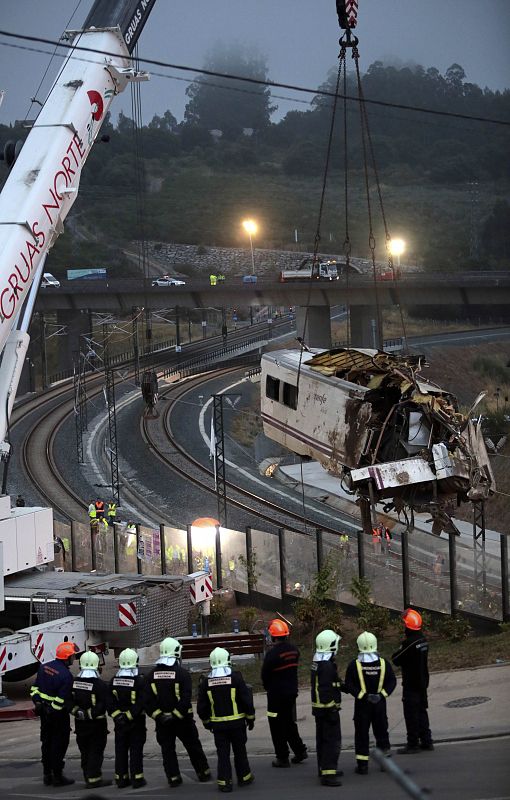 Un grupo de bomberos observa como una grúa retira uno de los vagones de las vías en el lugar del accidente.