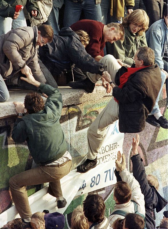 Los ciudadanos del oeste de Alemania Oriental se ayudan para subir el Muro de Berlín después de su apertura en noviembre de 1989.