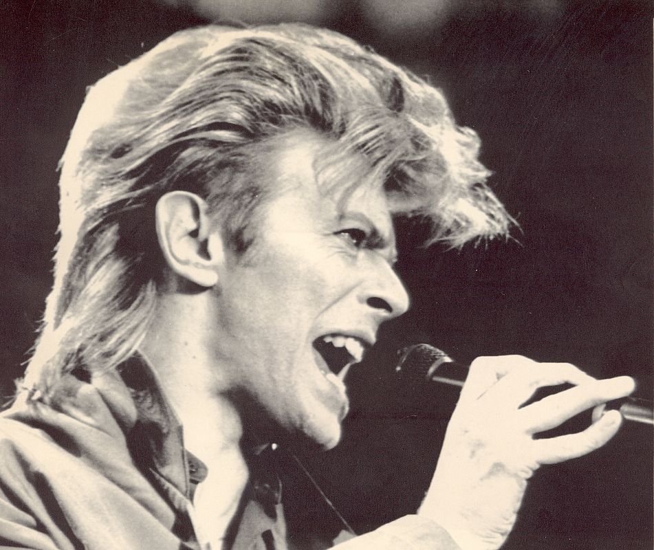 David Bowie de perfil cantando en un concierto.