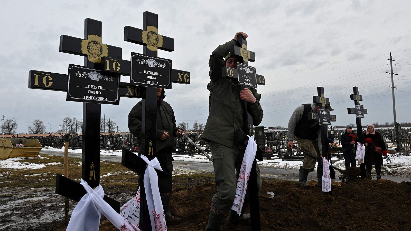 Los trabajadores de un cementerio colocan cruces en las tumbas de una familia de cinco personas