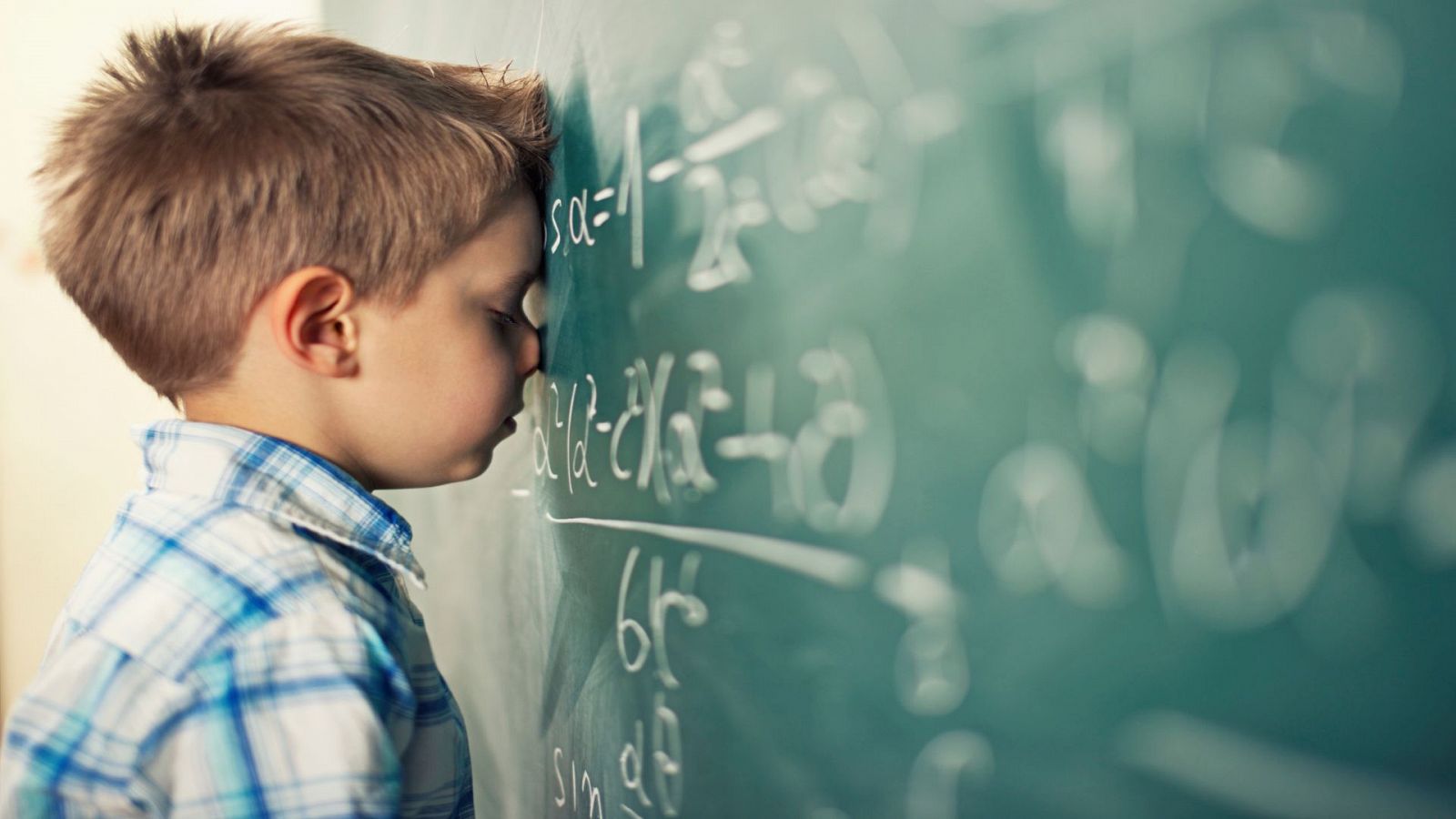 Imagen de un niño desesperado sobre la pizarra de un aula.