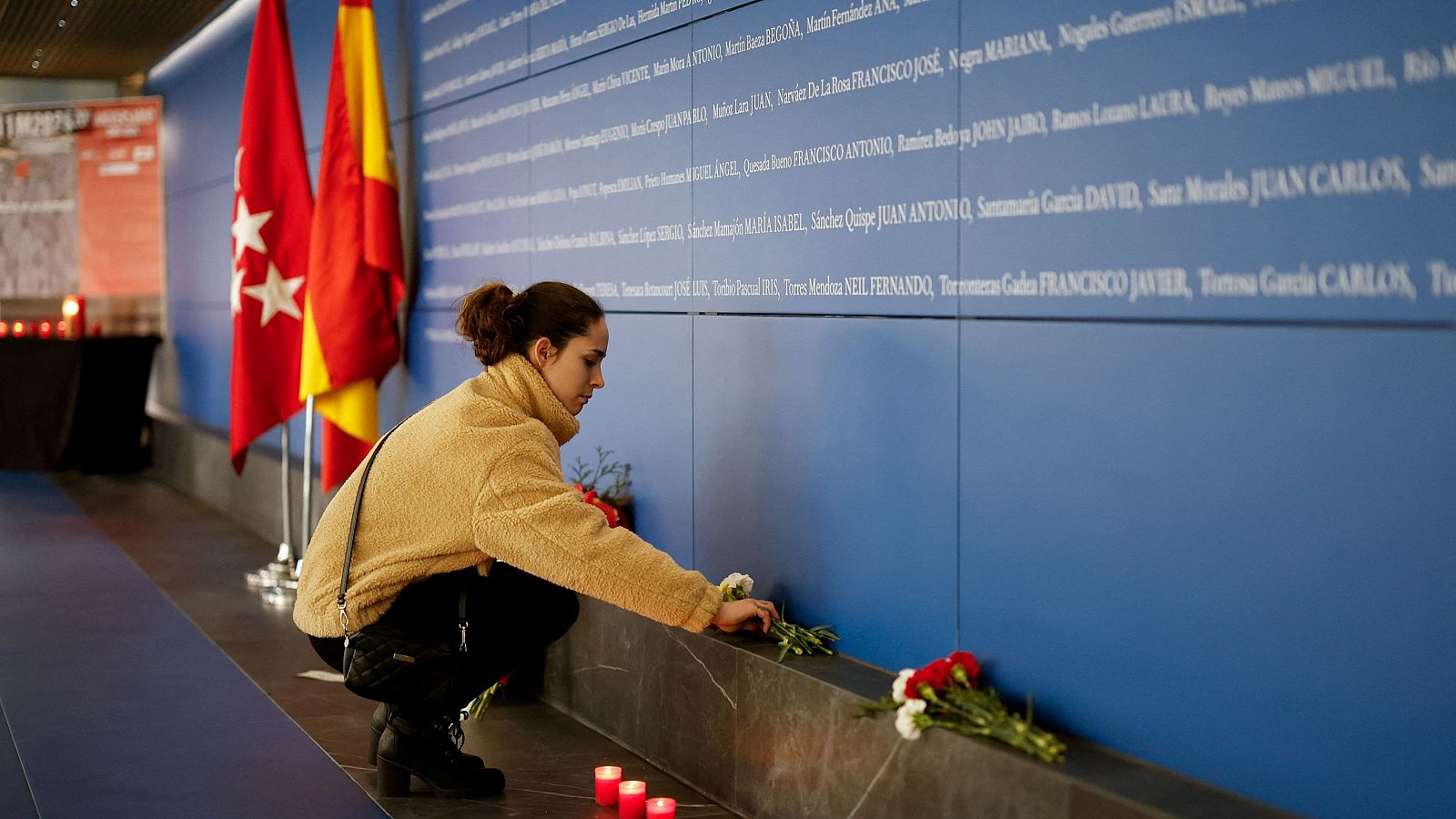 Una mujer deposita flores ante el panel instalado en Atocha con los nombres de las víctimas del atentado del 11M