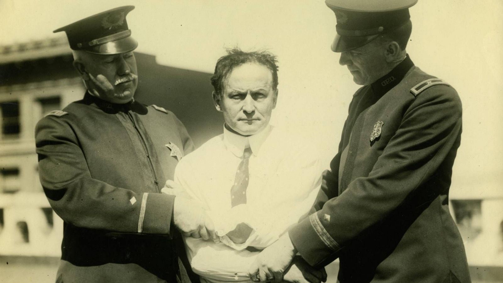 El gran Houdini, en uno de sus trucos de escapismo, escoltado por dos policías