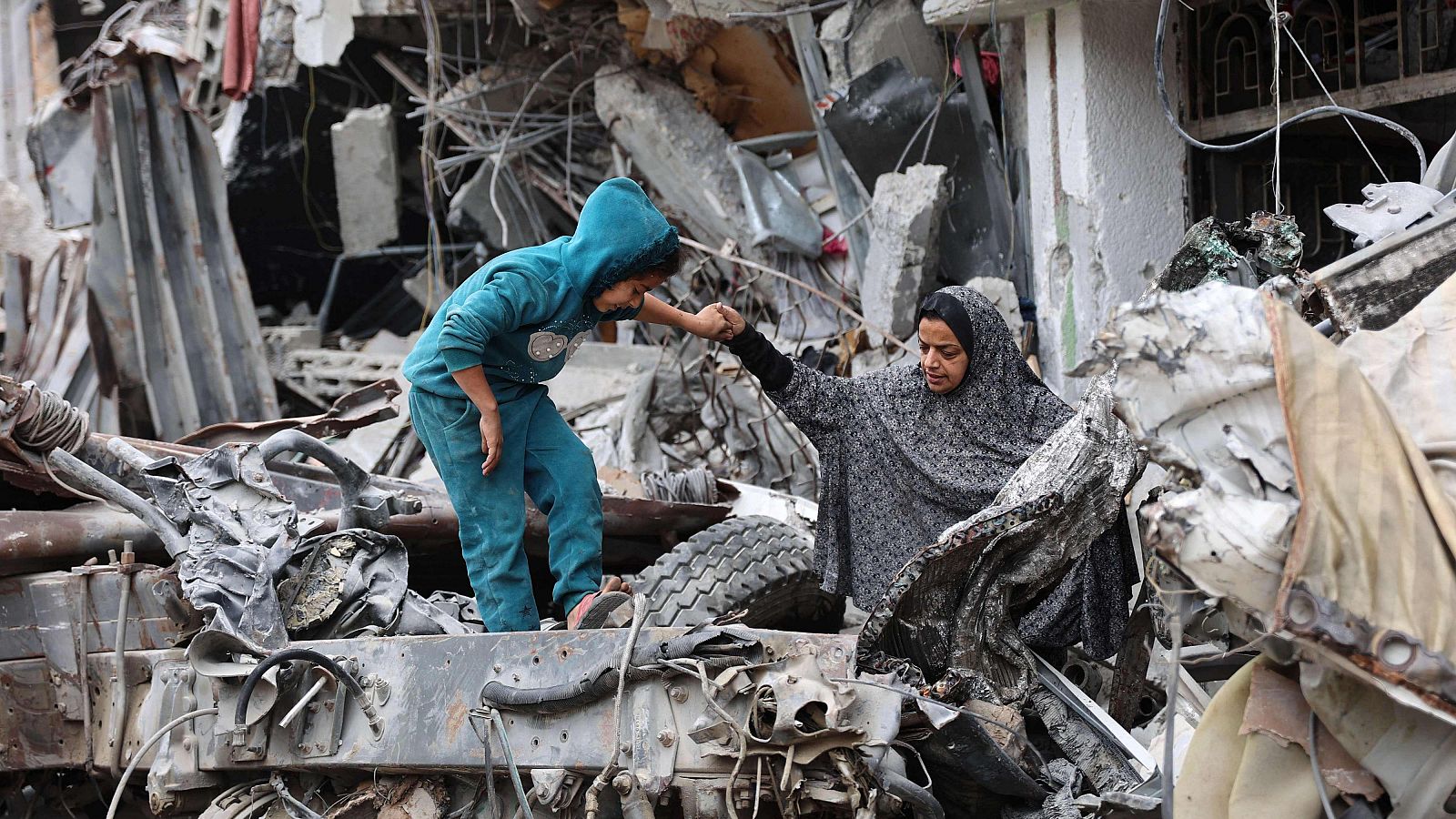 Una mujer palestina ayuda a un niño que juega sobre las ruinas de un edificio destruido por un bombardeo israelí