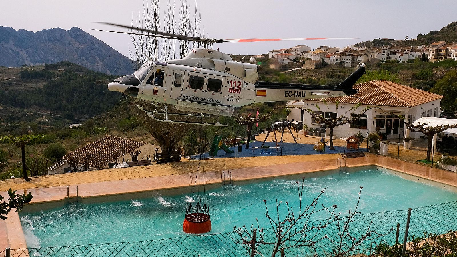 Un helicóptero de los Servicios de Emergencia carga agua en una piscina durante los trabajos de extinción del incendio forestal de Tárbena