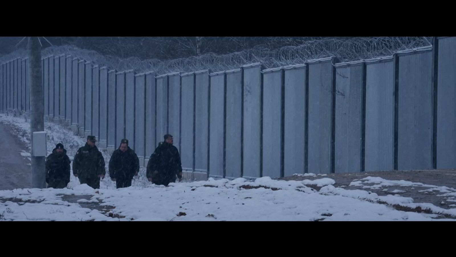 Cuatro policías con muro fronterizo de cemento y alambre