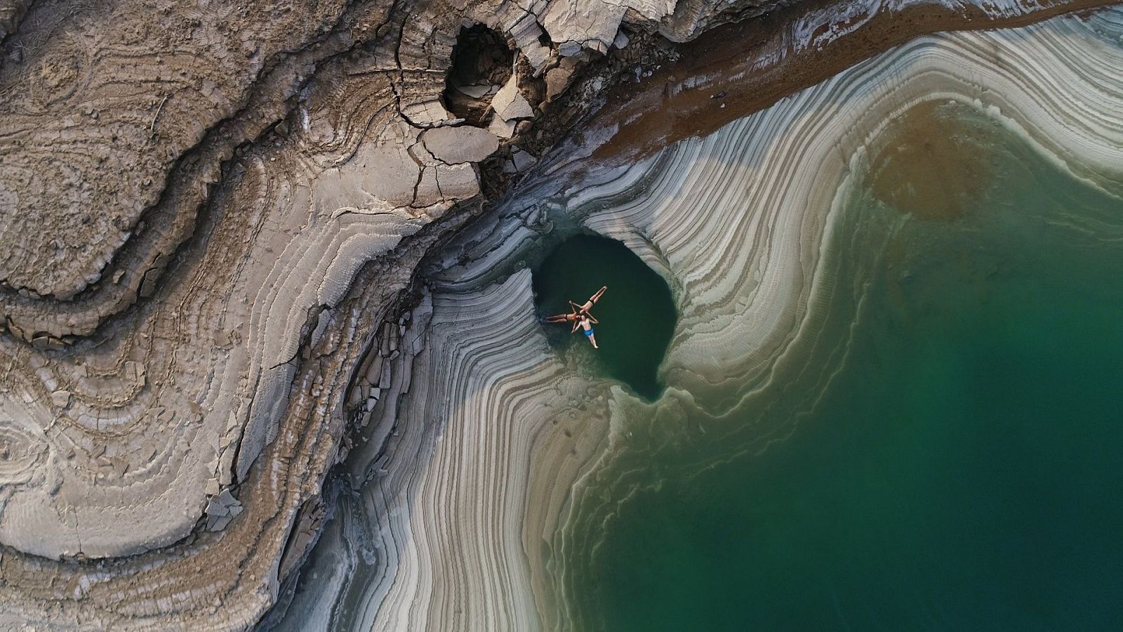 Imagen picado de tres hombres con las manos unidas en un lago rodeados de roca y sal