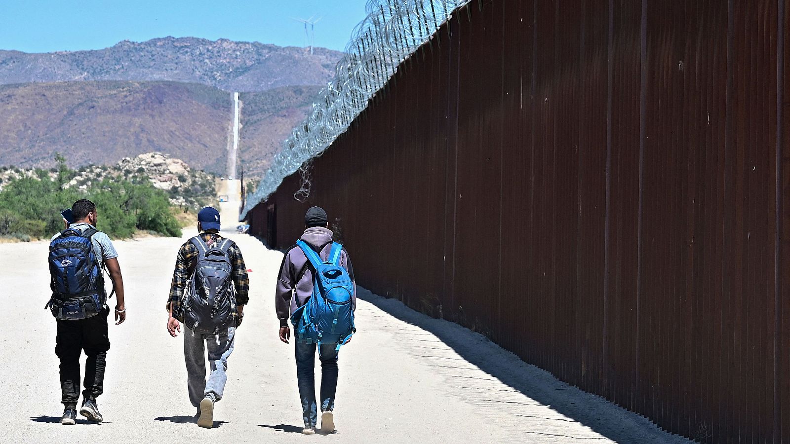 Varios migrantes caminan por el lado estadounidense del muro fronterizo en Jacumba Hot Springs, California, tras cruzar a pie desde México.