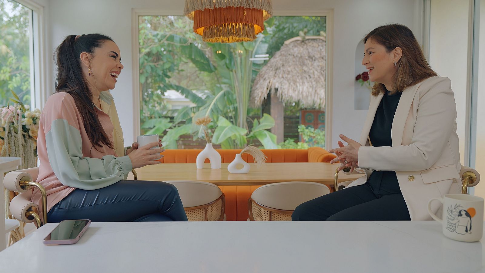 Beatriz y Chabeli sentadas en sillas altas de la cocina, con una encimera de fondo y una lampara que le da elegancia absoluta al espacio.