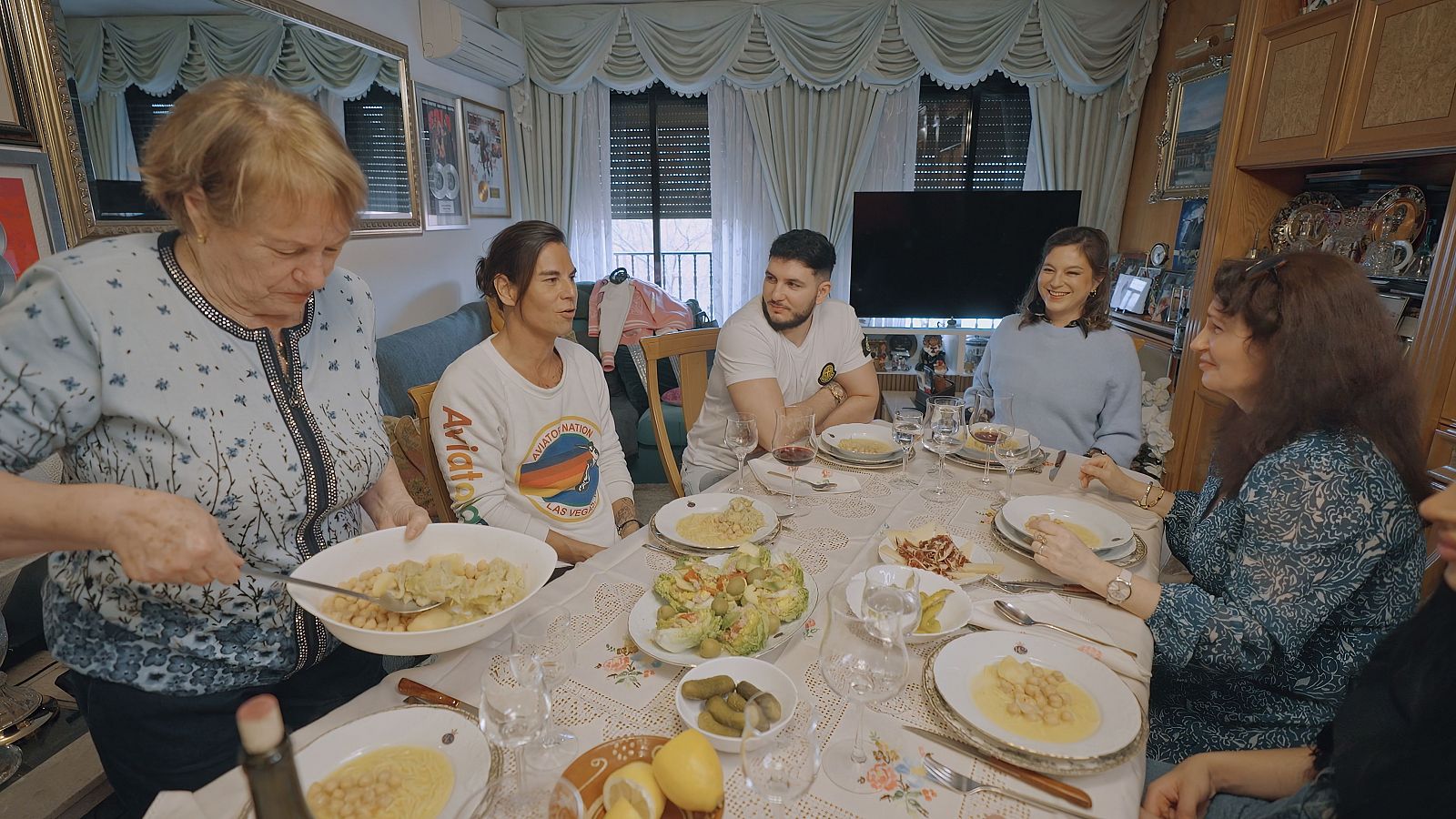 La familia de Omar y los hermanos estan juntos alrededor de una mesa, en casa de los abuelos de omar donde la decoración es tradicional y entrañable.