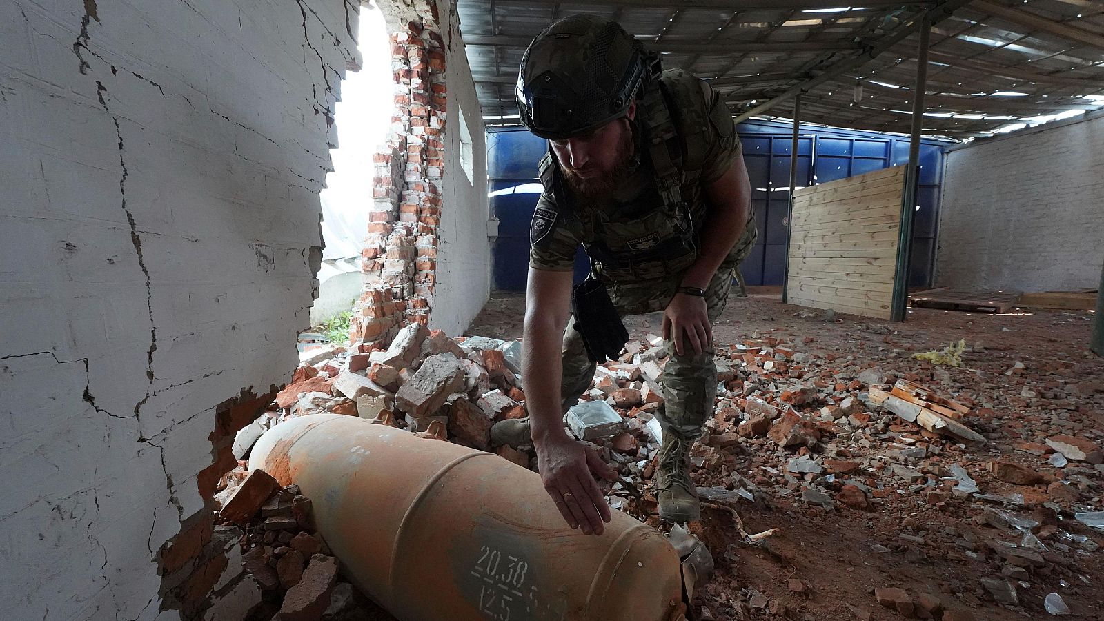 Un oficial de policía ucraniano inspecciona una bomba sin detonar de 250 kilogramos después de un ataque aéreo ruso a un almacén agrícola