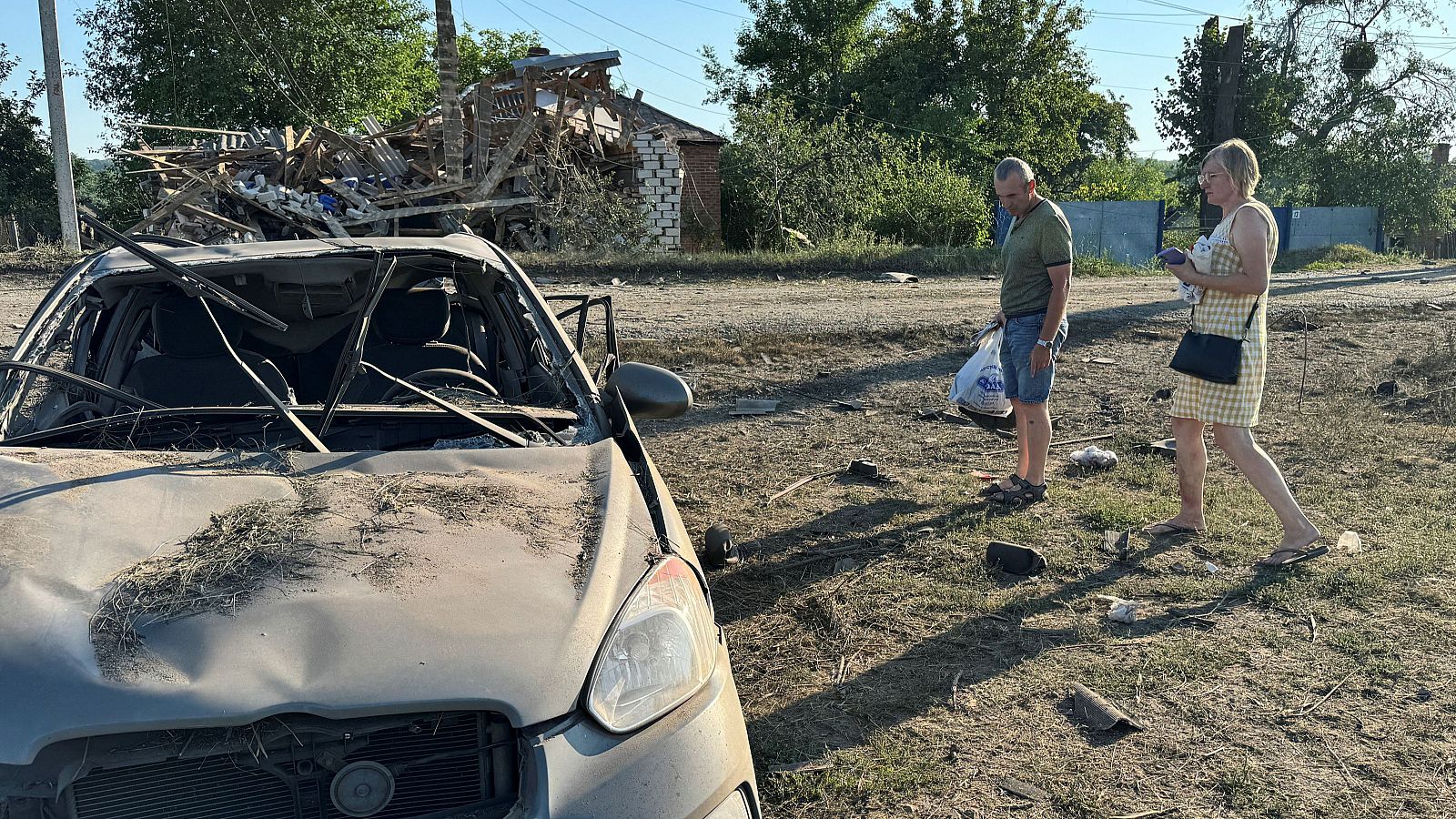 Dos personas junto a un coche dañado en un bombardeo ruso en la localidad de Budy, en la región de Járkov