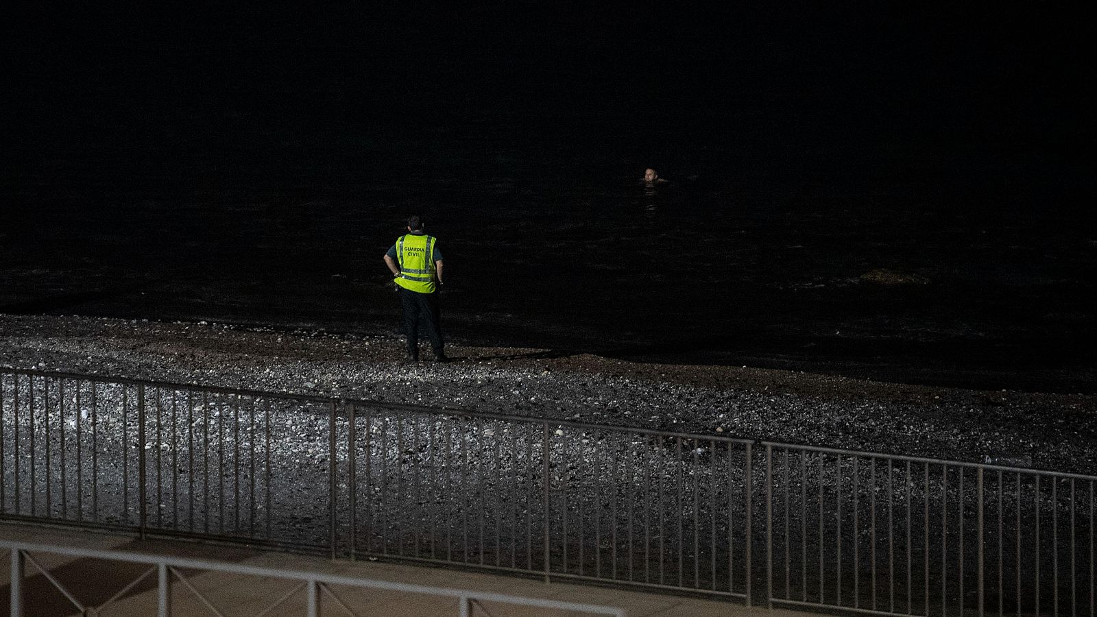 Un agente de la Guardia Civil espera la entrada a nado de un joven por la playa del Tarajal