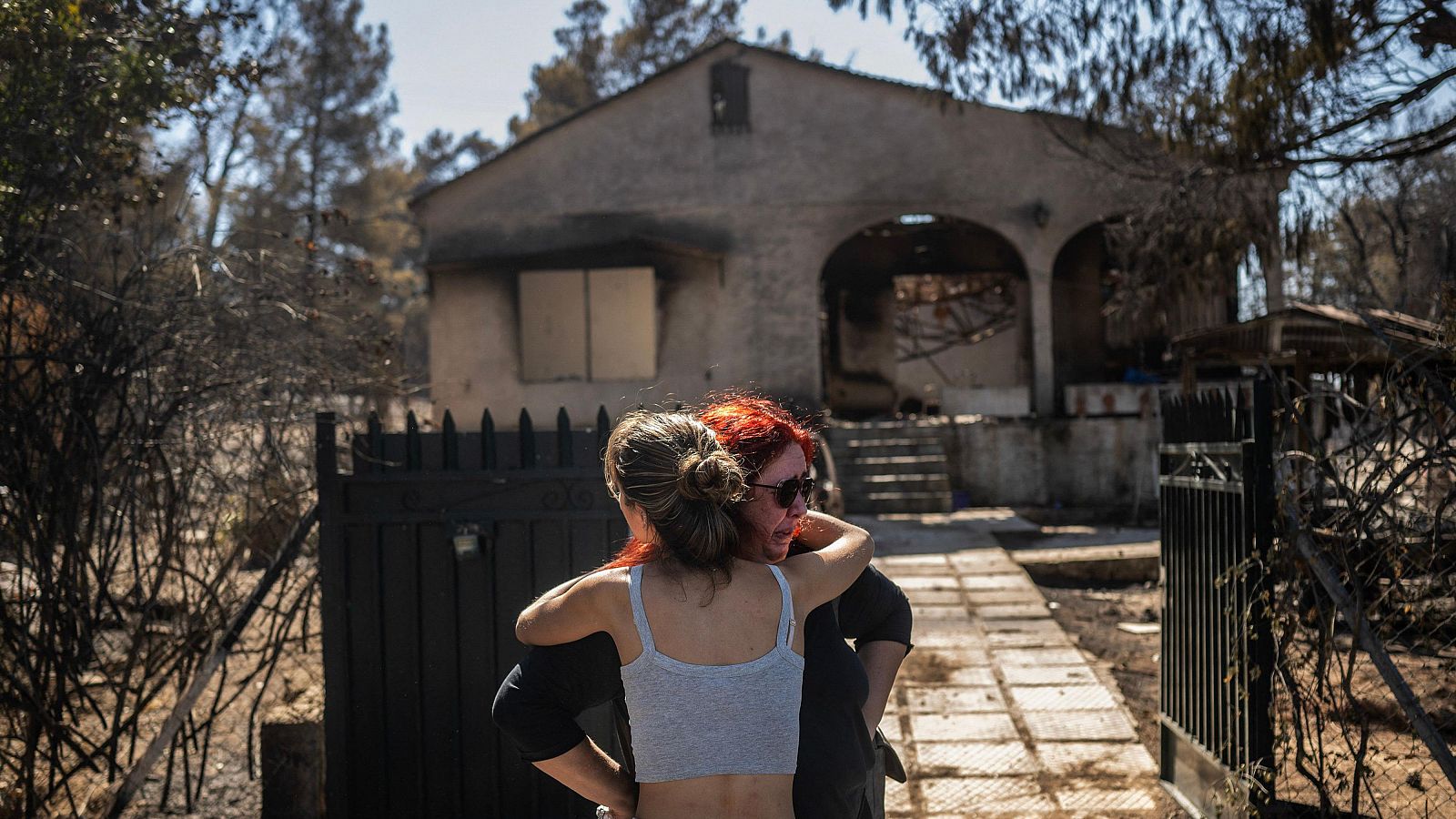 Unos familiares se consuelan mutuamente frente a su casa calcinada por el incendio que ha afectado a los suburbios de Chalandri. Continúan por cuarto día consecutivo los esfuerzos por frenar los fuegos que cercan Atenas.