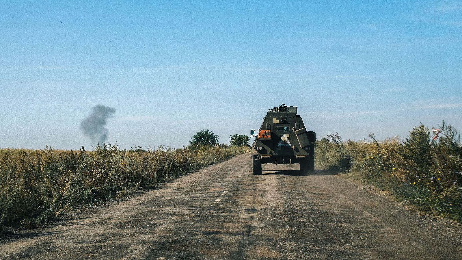 Un vehículo blindado circula por una carretera mientras el humo se eleva por una explosión