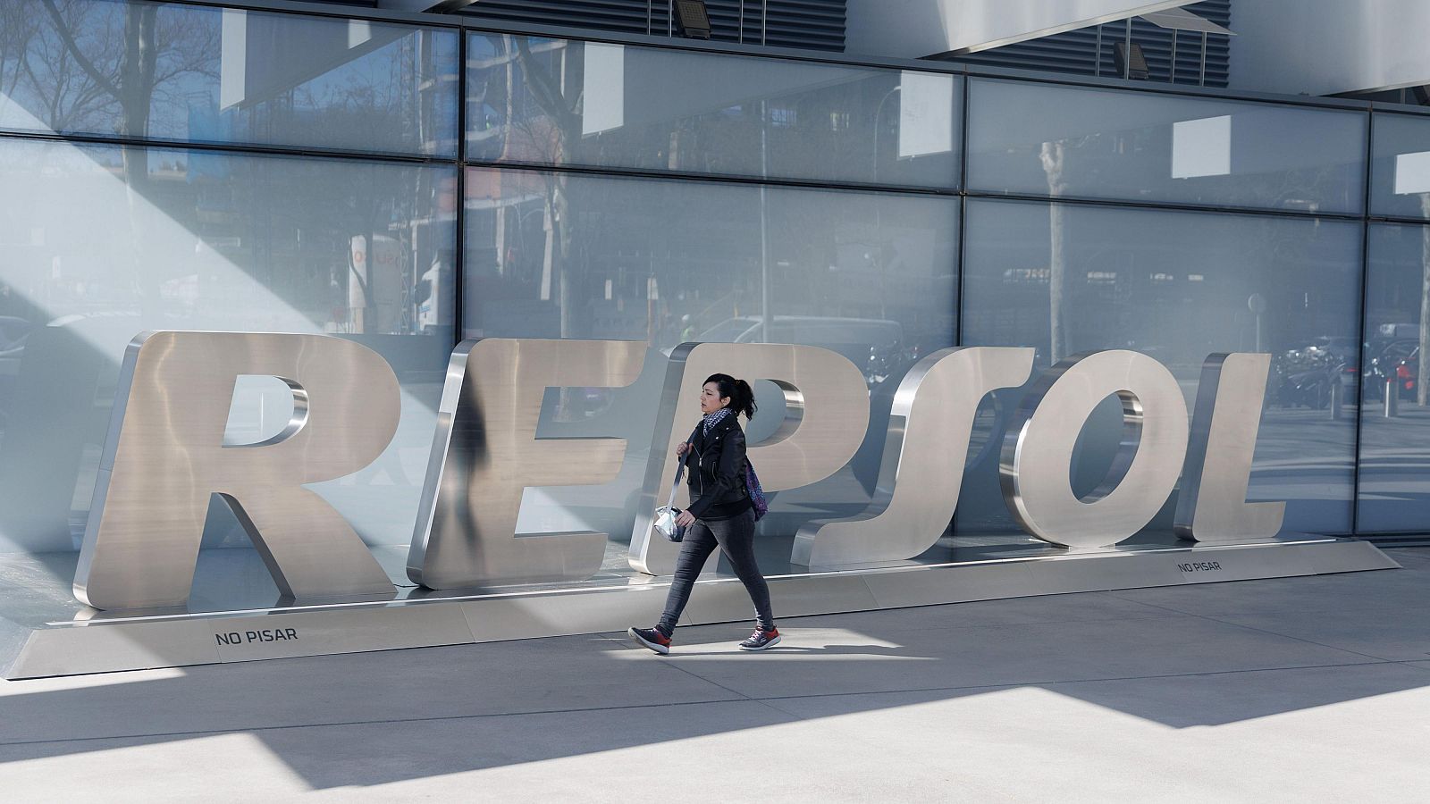 Una mujer camina frente a las letras Repsol en su sede