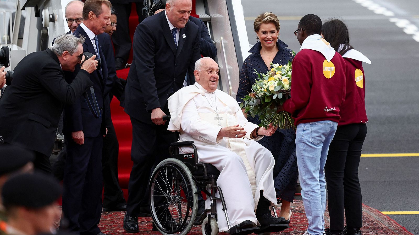 El Gran Duque Enrique de Luxemburgo, la Gran Duquesa María Teresa y el primer Ministro Luc Frieden acompañan al Papa Francisco mientras recibe flores en el aeropuerto de Luxemburgo durante un viaje apostólico de un día a Luxemburgo el 26 de septiembre de 2024.