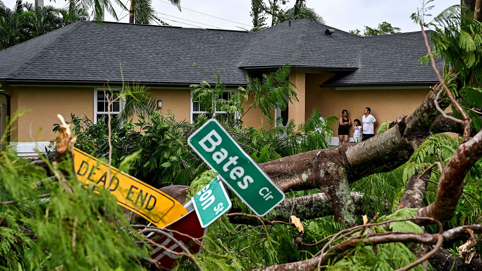 Una familia fuera de su casa ante los restos de un árbol caído en Fort Myers, Florida