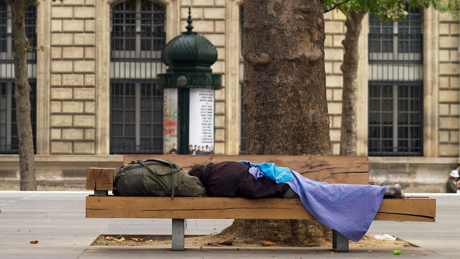 Una persona duerme en un banco en plena calle